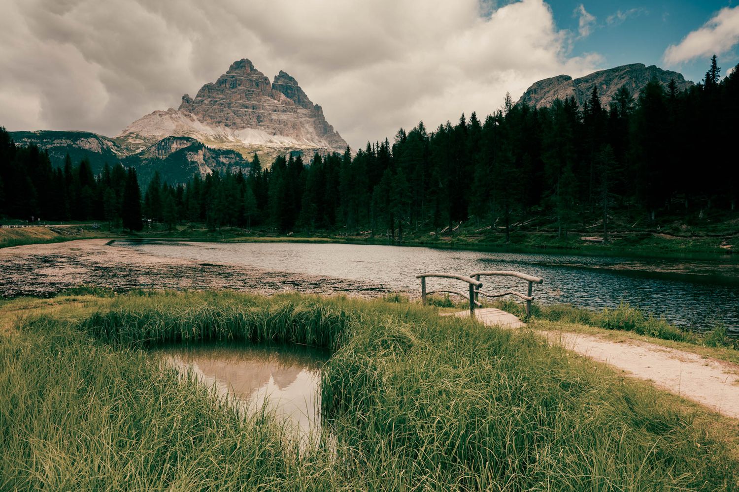 Dramatic Dolomite mountains with jagged rocky peaks, winding road, and moody overcast sky in the Italian Alps.