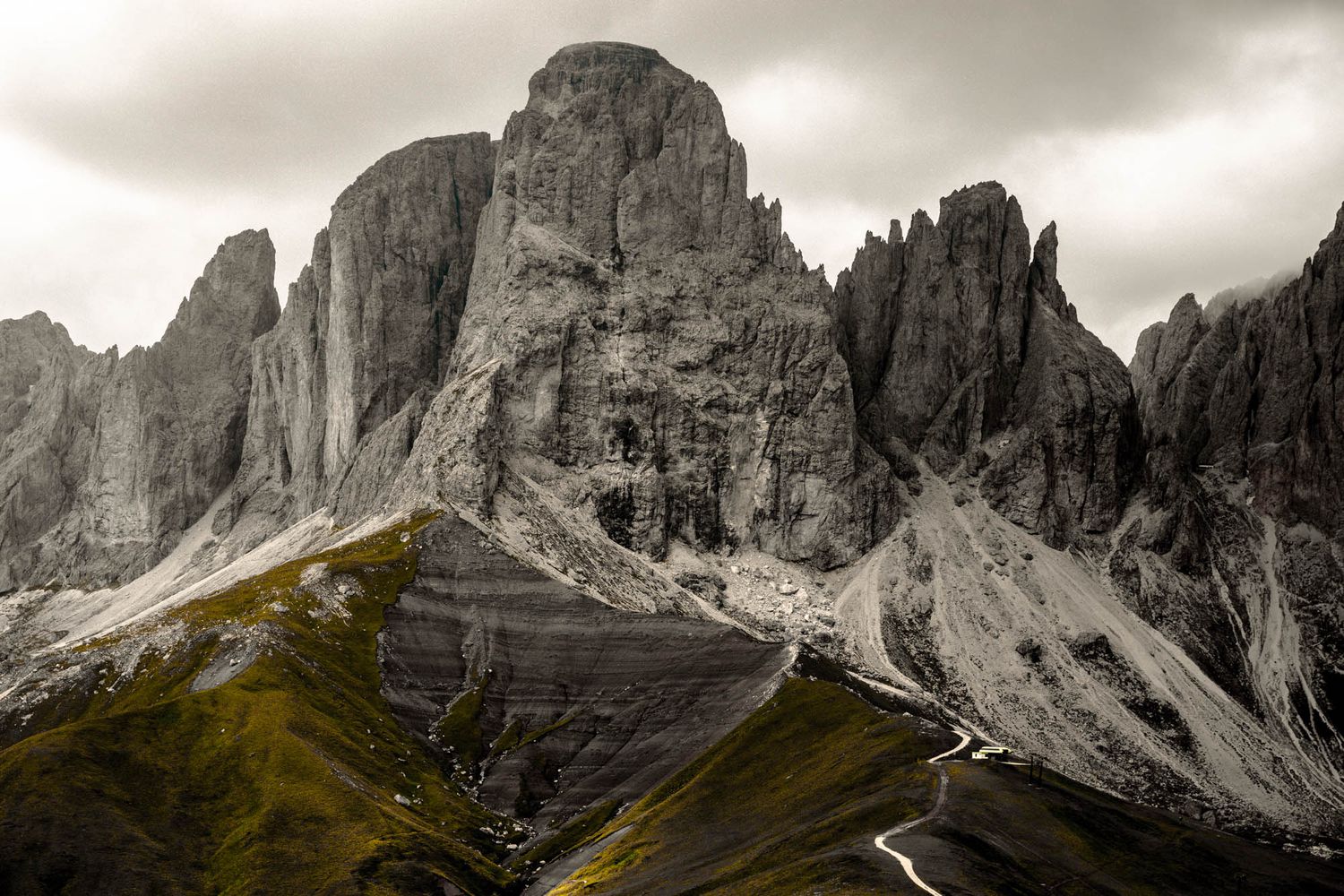 Dramatic Dolomite mountains with jagged rocky peaks, winding road, and moody overcast sky in the Italian Alps.