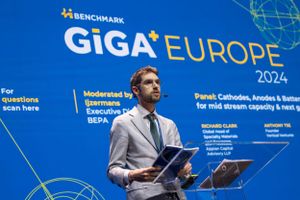 Eventfotography of a speaker presenting at the GiGa Europe 2024 conference wearing a gray suit against a blue backdrop with event branding.