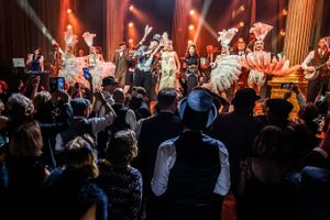Eventfotography of energetic performers on stage entertain a packed crowd at a lively concert venue with dramatic red lighting.