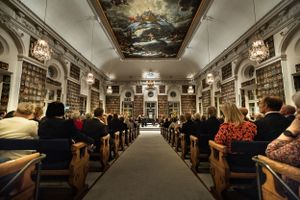 Eventfotography of a people seated in wooden pews inside riddarhuset with a painted ceiling and grand architecture.