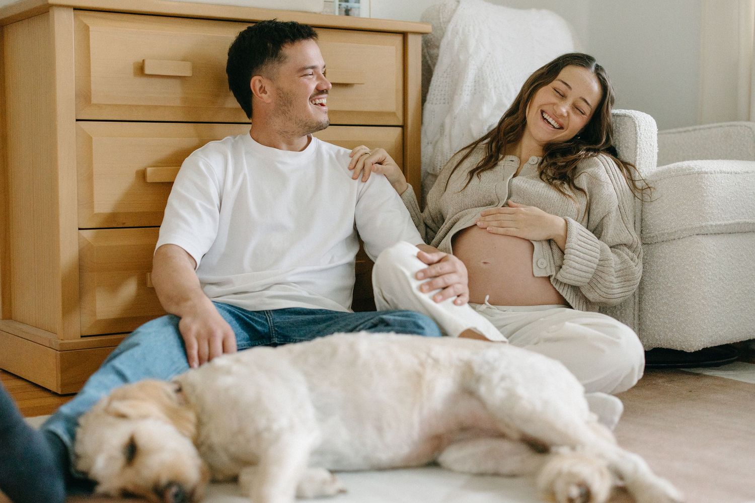 man and pregnant woman sitting on the ground of their nursery with dog