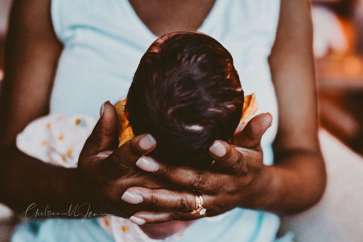 A mother tenderly cradles her newborn baby's head in her hands, captured in a warm, intimate portrait.