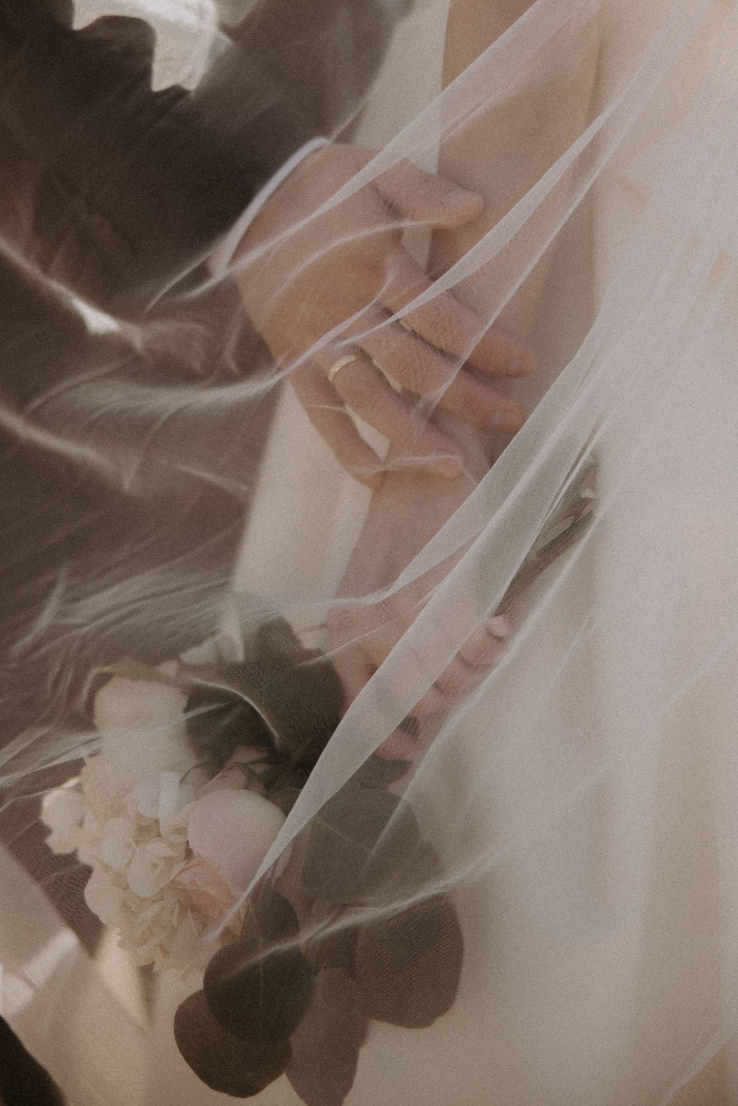 An ethereal shot of a bride and groom holding hands with a bouquet, seen through a sheer wedding veil.