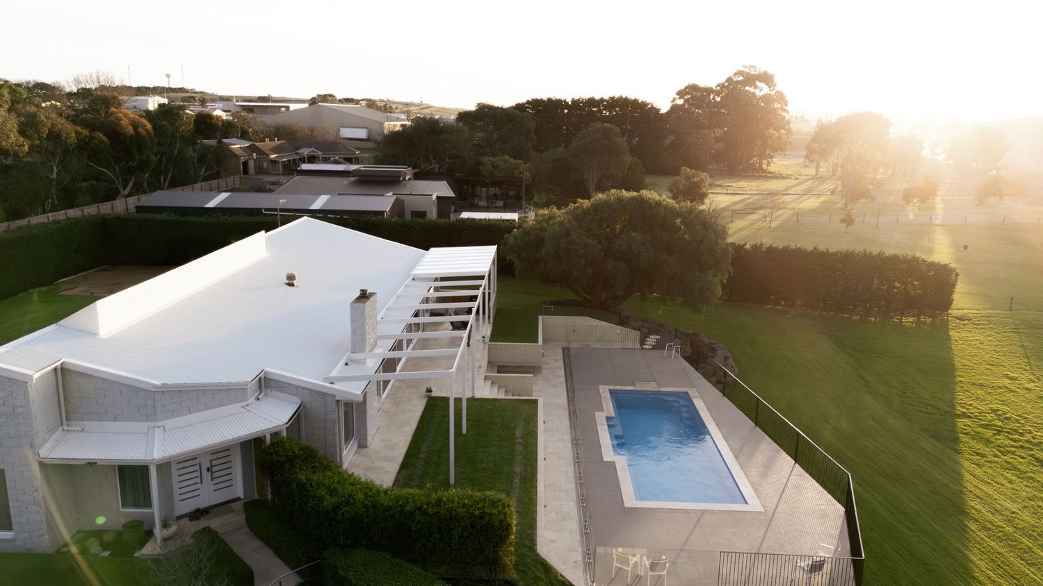 Modern white luxury villa with infinity pool and manicured lawn at sunset showcases contemporary architectural design. Warrnambool