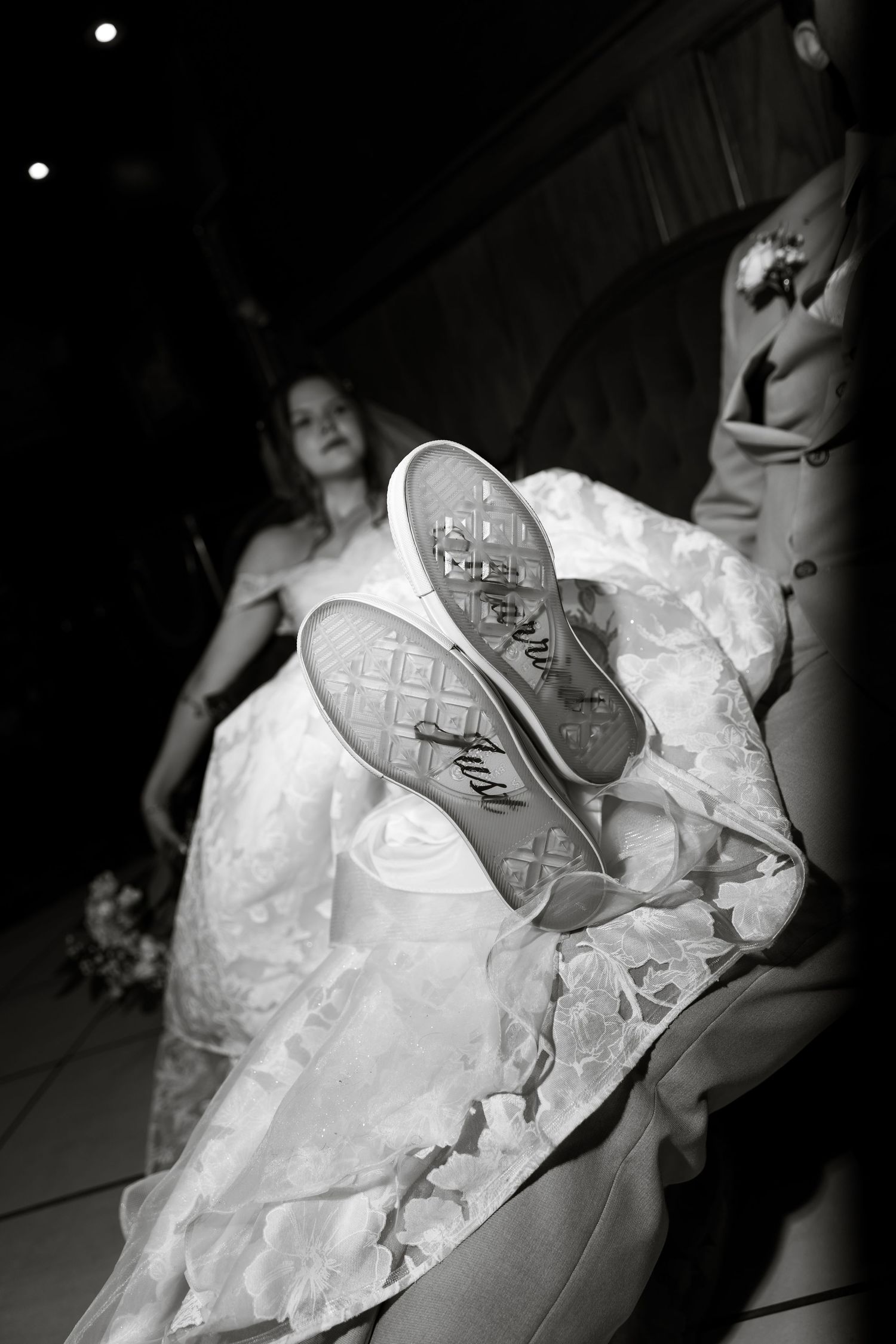 Black and white photo of bride showing custom wedding sneakers with writing on soles during wedding ceremony.