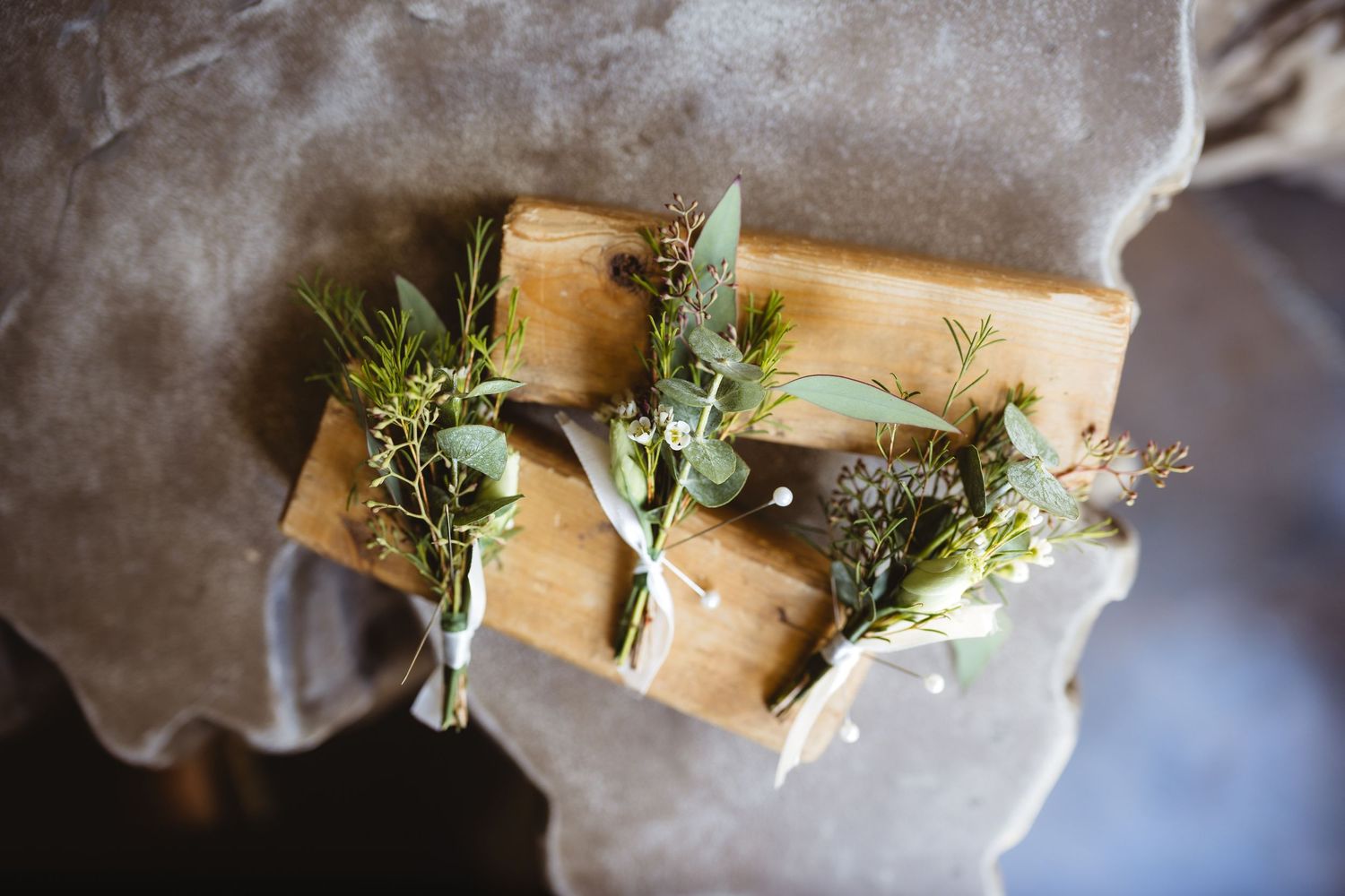 Rustic wedding boutonnieres with eucalyptus and greenery resting on wooden blocks, perfect for a natural boho wedding.