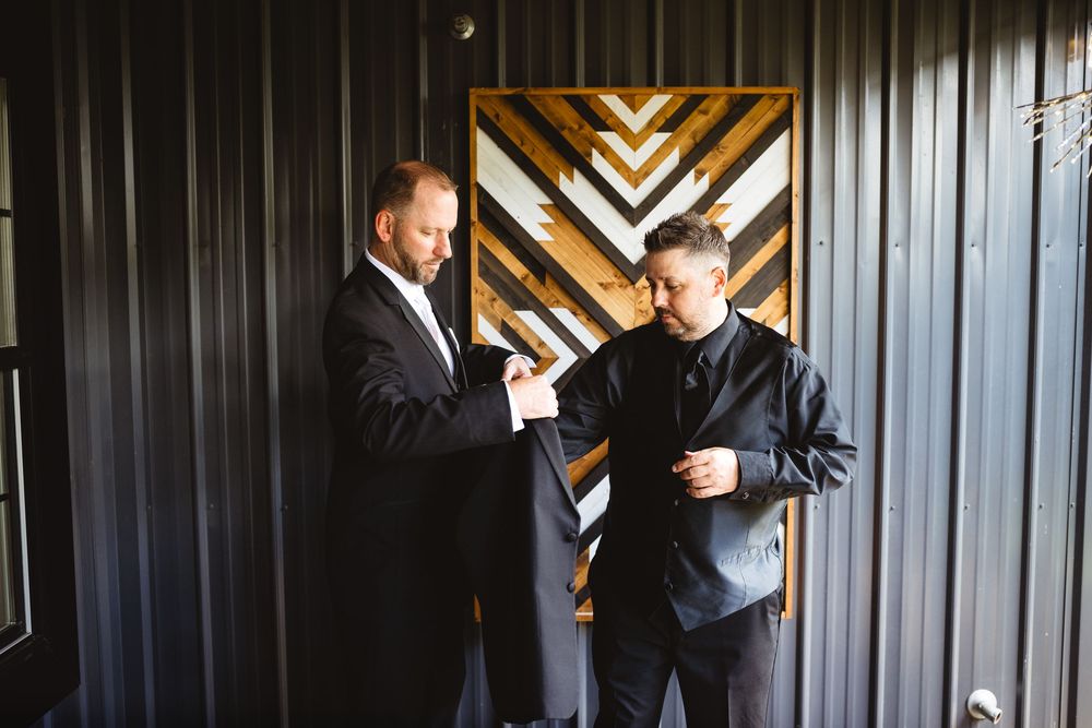 Two men in formal suits conversing indoors near a decorative wooden chevron wall panel.