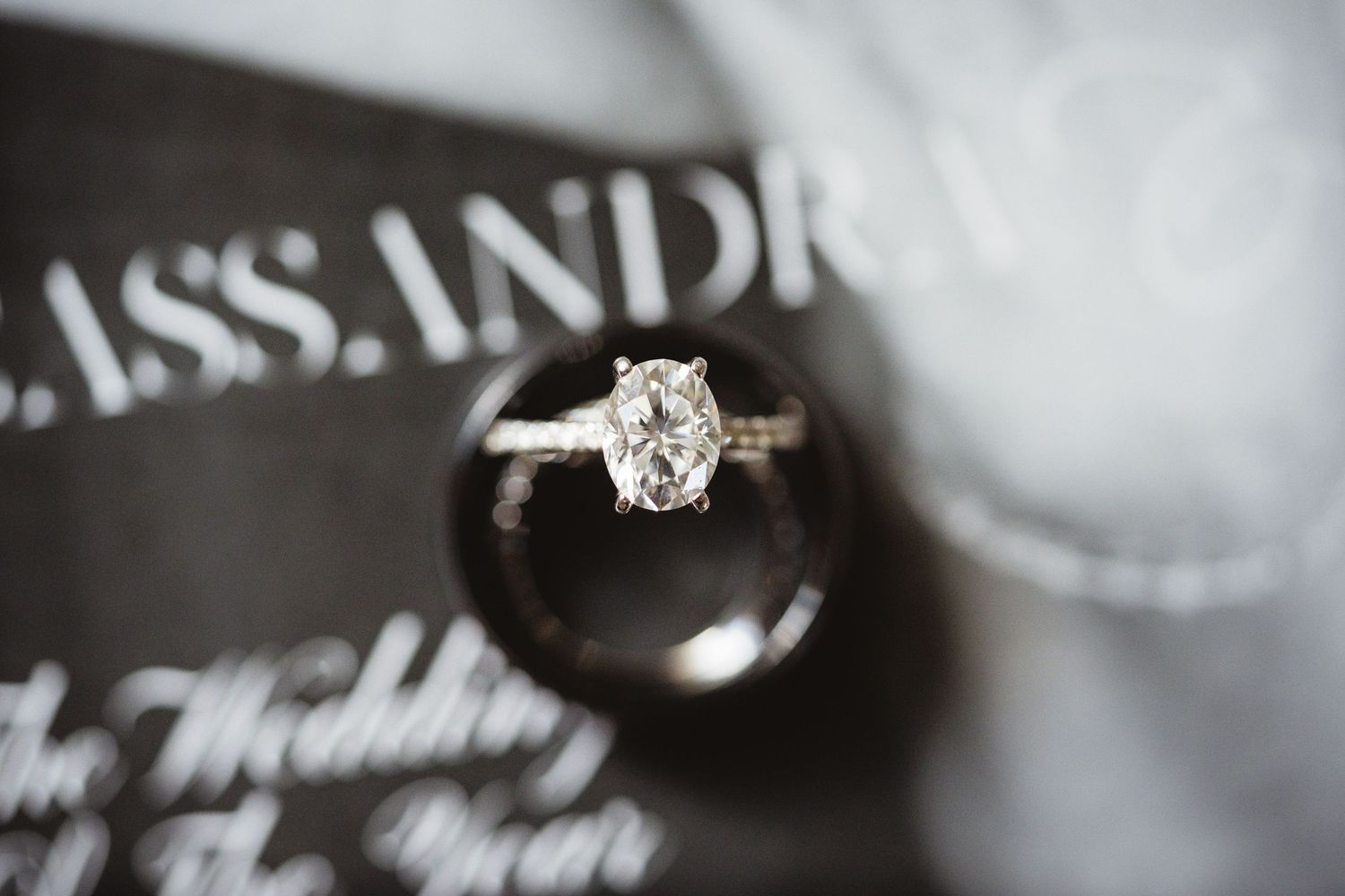 Elegant oval diamond solitaire engagement ring resting on a wedding invitation with cursive script.