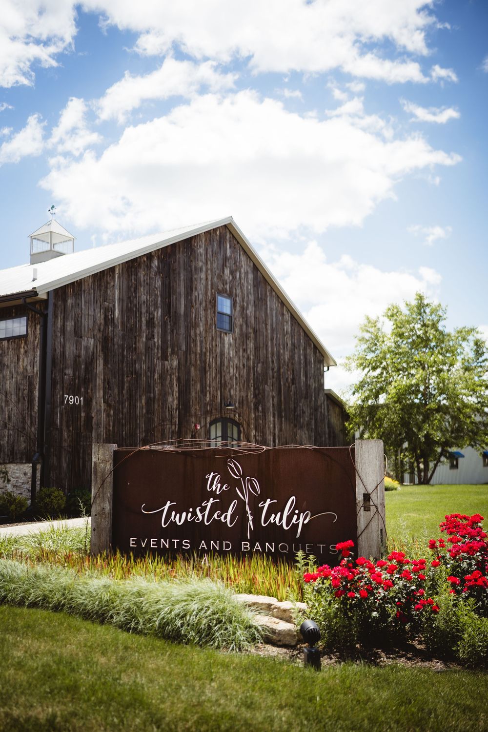 Twisted Tulip Events and Banquet venue rustic barn exterior with red roses and blue sky in background.