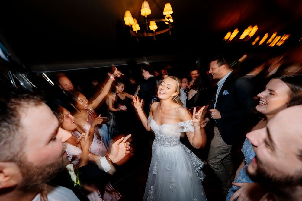 Bride in white gown dancing joyfully with guests at a lively wedding reception party.
