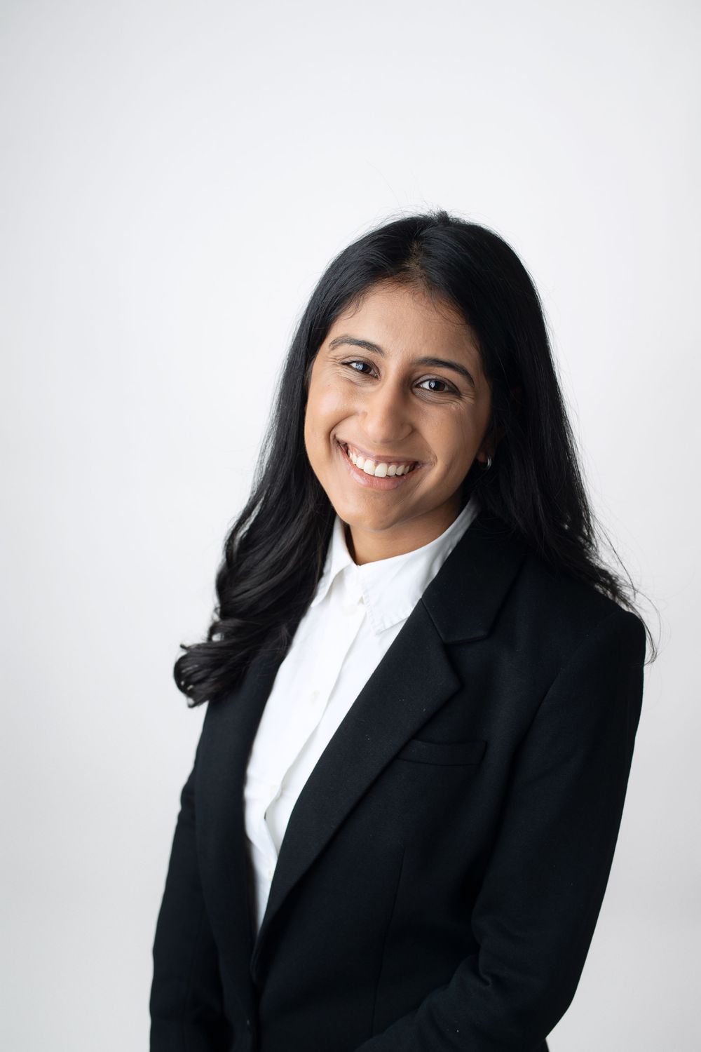 Professional woman in black blazer and white shirt smiles confidently against white background.