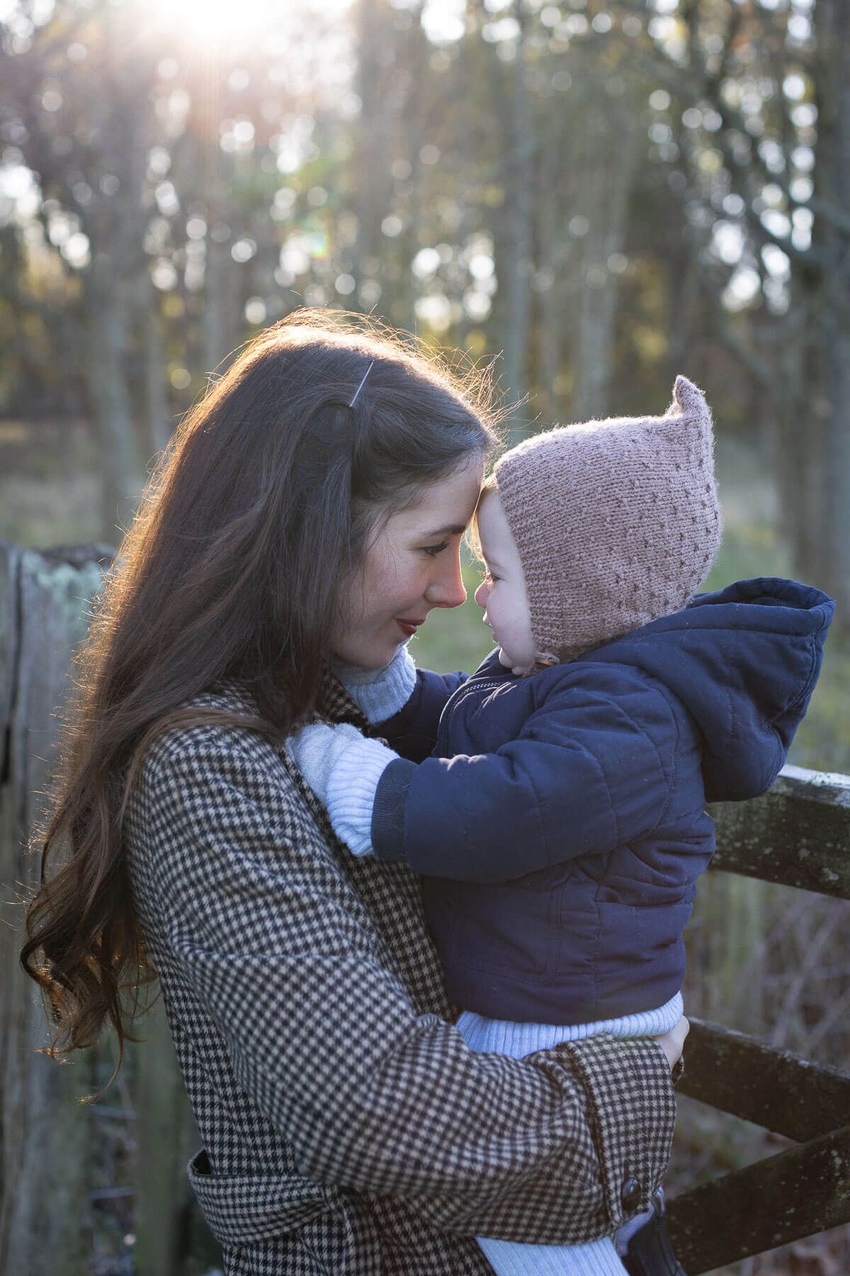 A mother tenderly holds her baby outdoors, touching foreheads in an outdoor family photography session in Sussex woodland