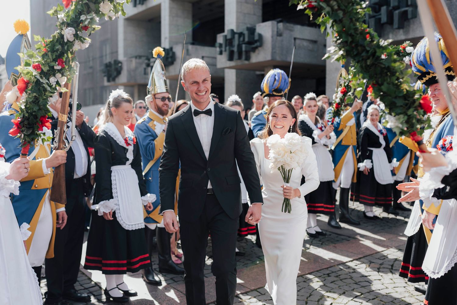 Bride and groom walk through a traditional folk dance guard of honor at their outdoor wedding ceremony.