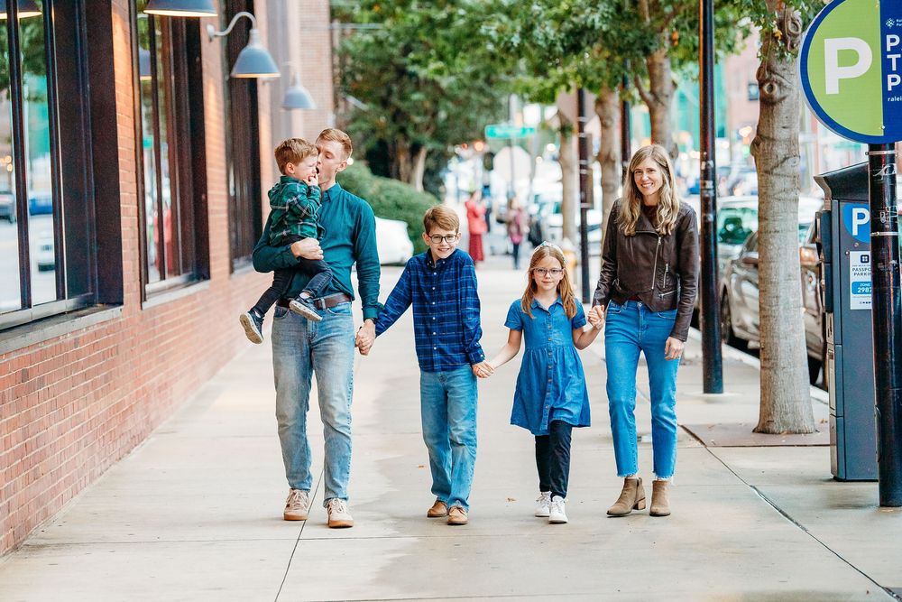 Happy family of five walking hand in hand on a city sidewalk in coordinating blue outfits.