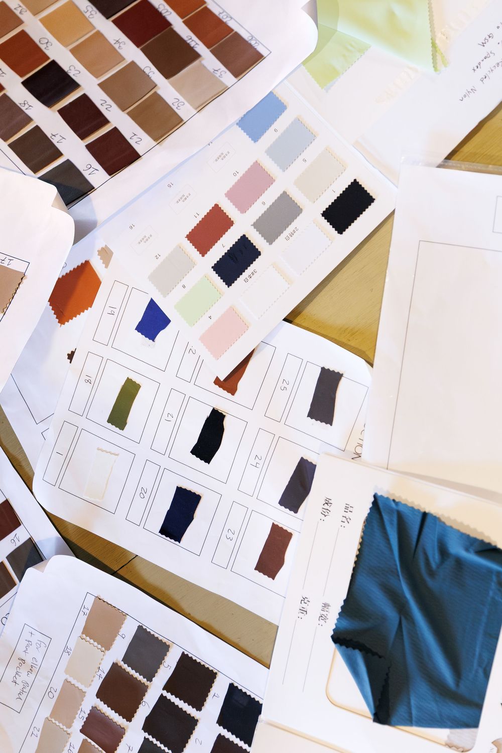 Fabric color swatches and sample books spread on a table for textile design selection.
