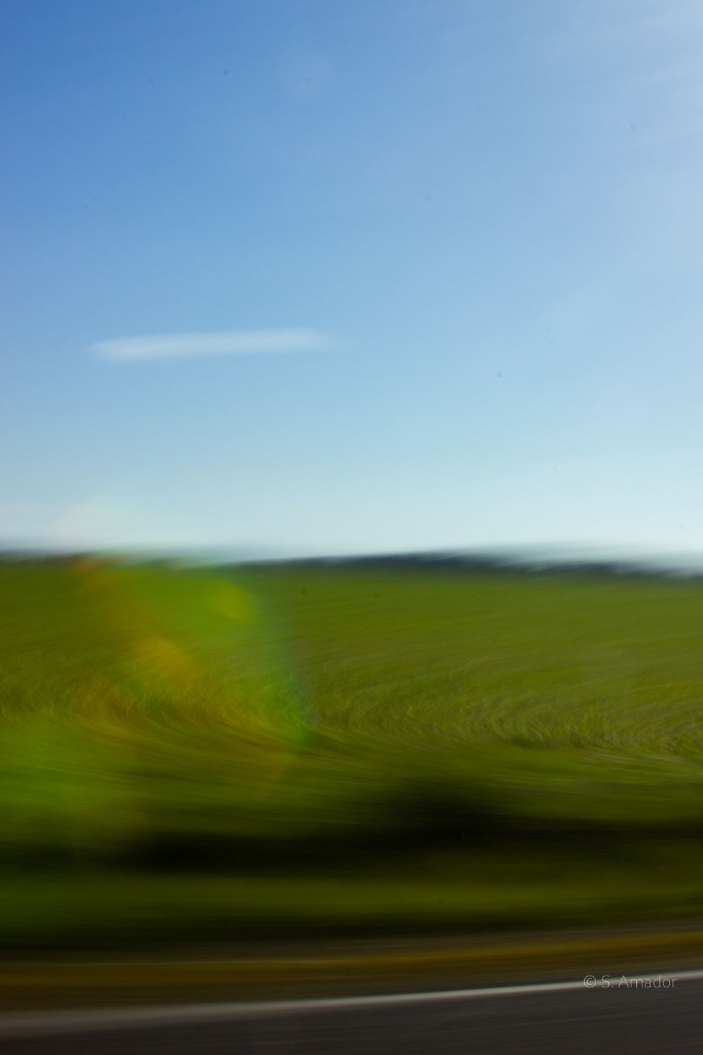 Blurred motion shot of green rolling hills and farmland under a clear blue sky taken from a moving vehicle.