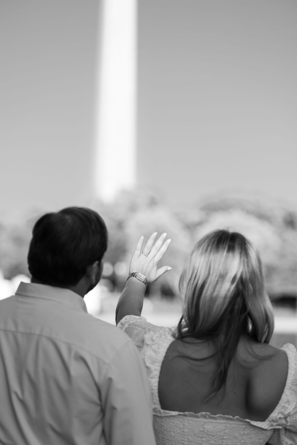 Black and white photo of a couple viewed from behind, woman waving near the Washington Monument.