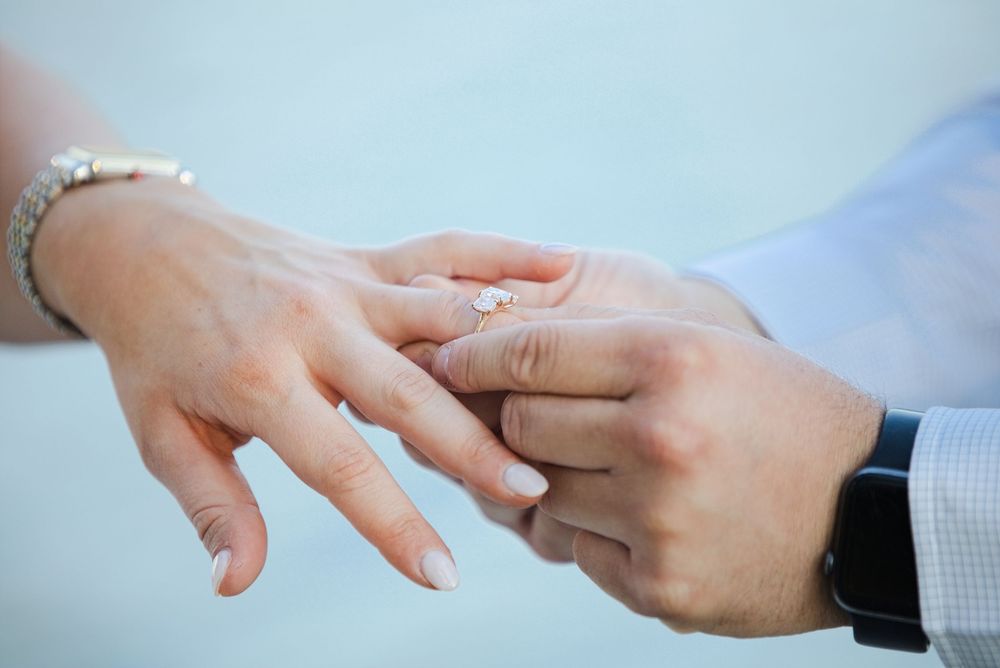 Close-up of a man placing a diamond engagement ring on a woman's finger during a marriage proposal.