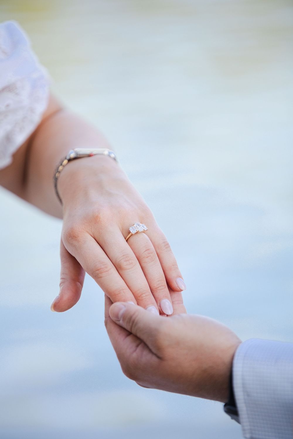 Close-up of a woman's hand wearing a diamond engagement ring and bracelet, held gently by a man's hand.