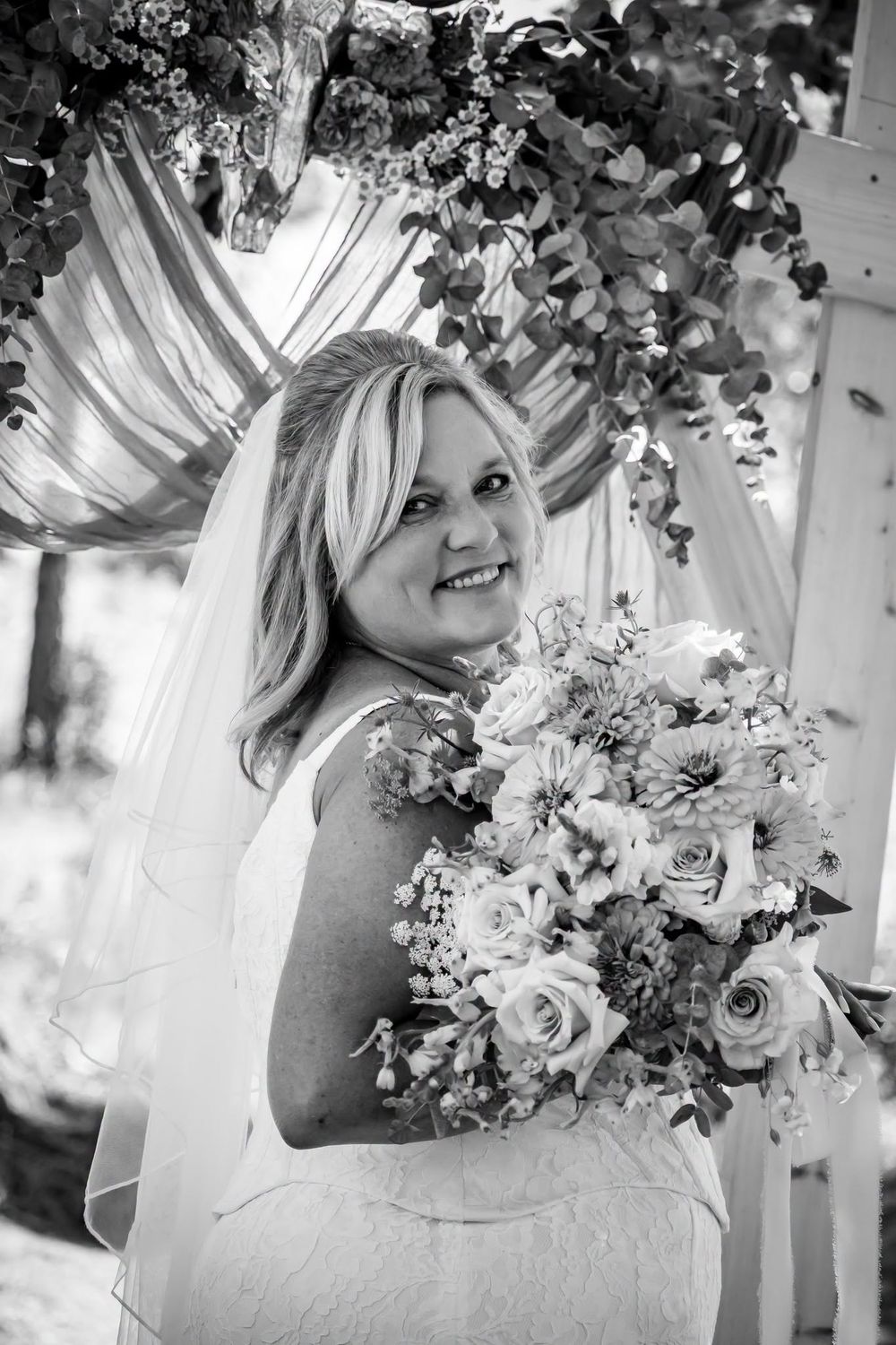 A bride under her wedding arch decorated by Hometown Wedding Co.