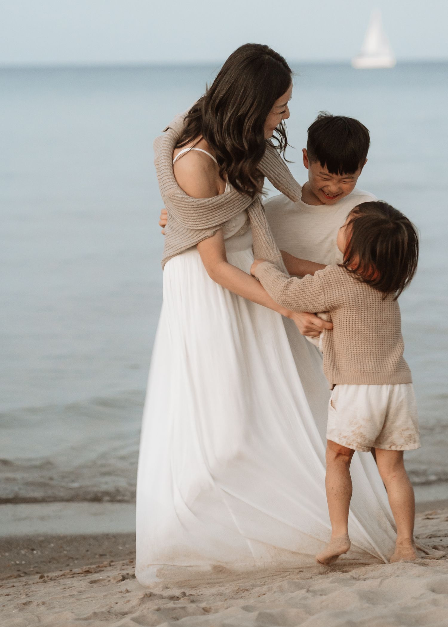A family in white clothing explores the beach shoreline together at sunset as waves gently roll during a beach mini session at Gillson Beach