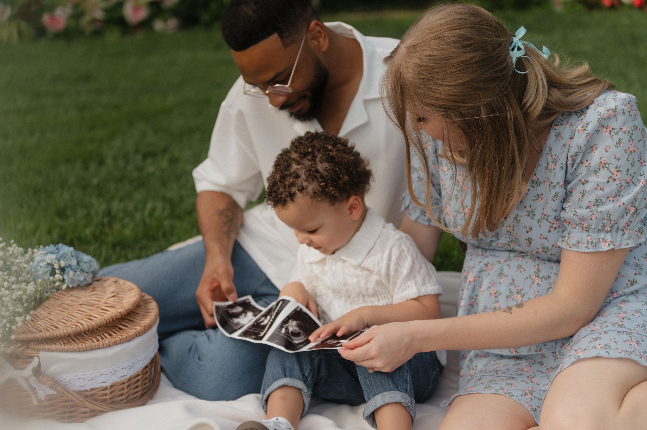 People sitting outdoors on grass looking at a photo album together on a sunny afternoon.