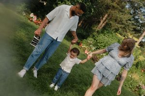 Three people walking together outdoors on a sunny day while holding hands through a green garden space.