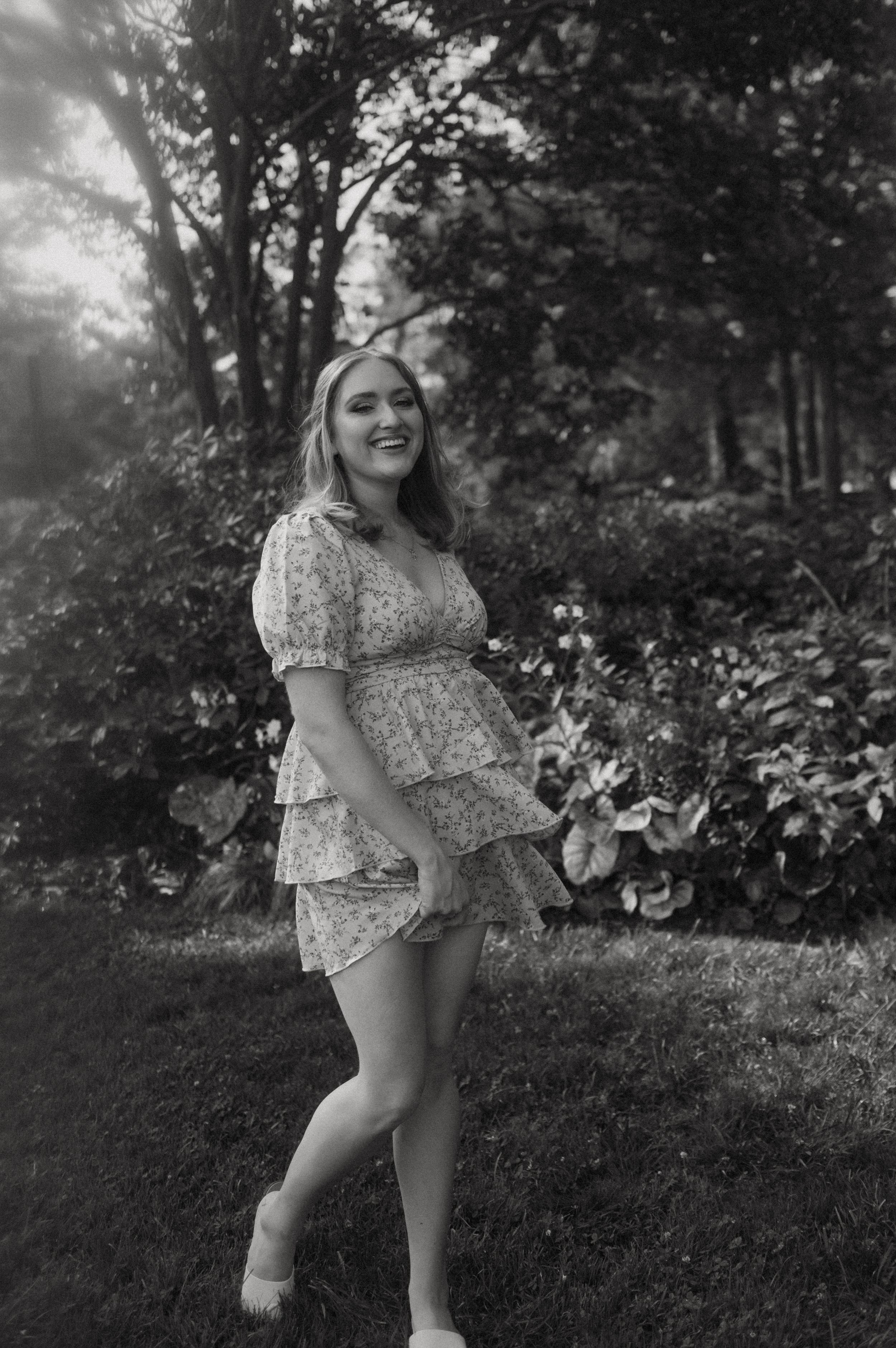A young person in a floral dress spins and plays in an outdoor garden setting captured in black and white.