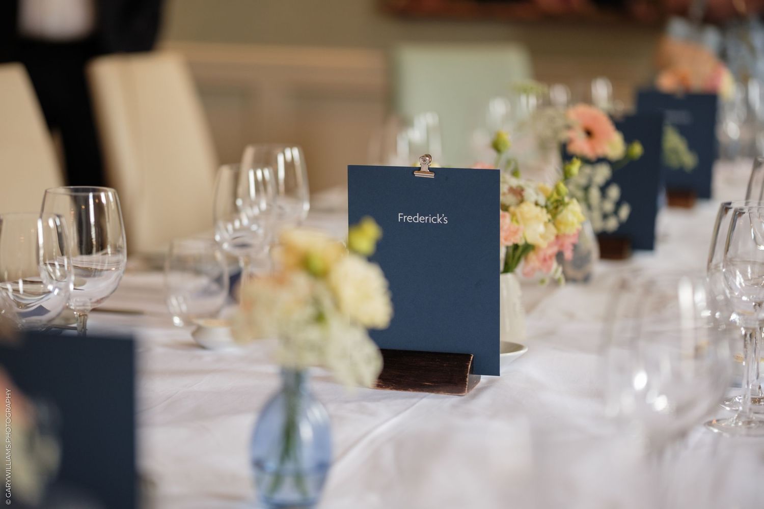 Elegant wedding reception table setting with navy blue place cards, white linens, and delicate floral centerpieces.