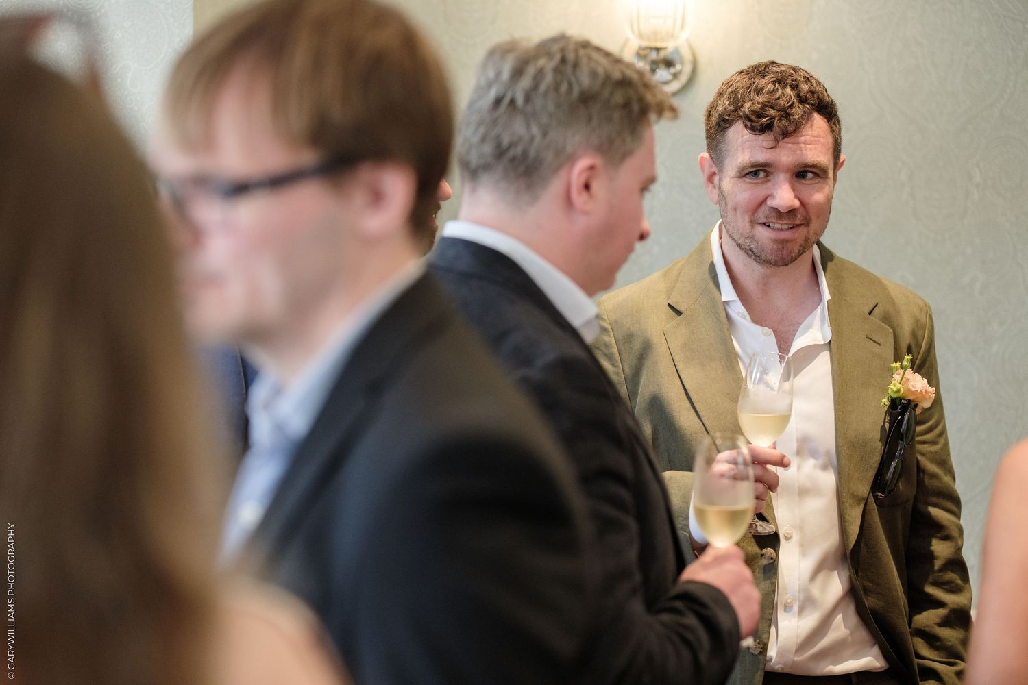 Men in suits socializing at a formal event, holding champagne glasses in an elegant venue.