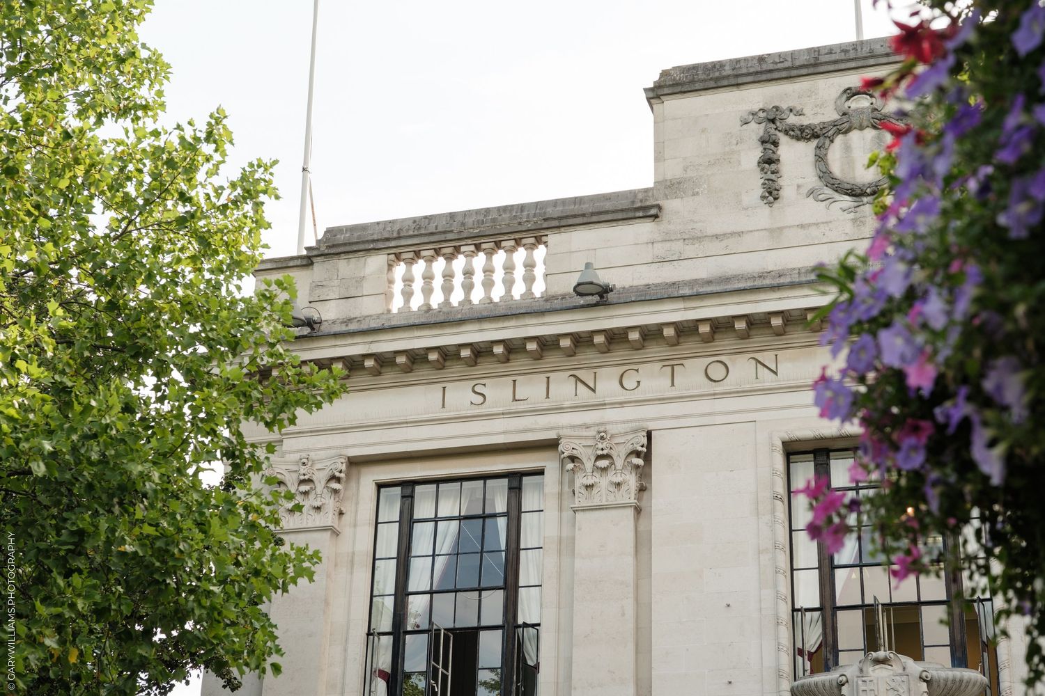Historic Islington Town Hall building facade with ornate architecture, surrounded by trees and purple flowers.
