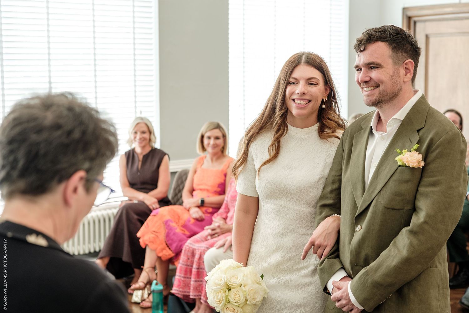 Bride and groom smiling during wedding ceremony with guests seated in background.
