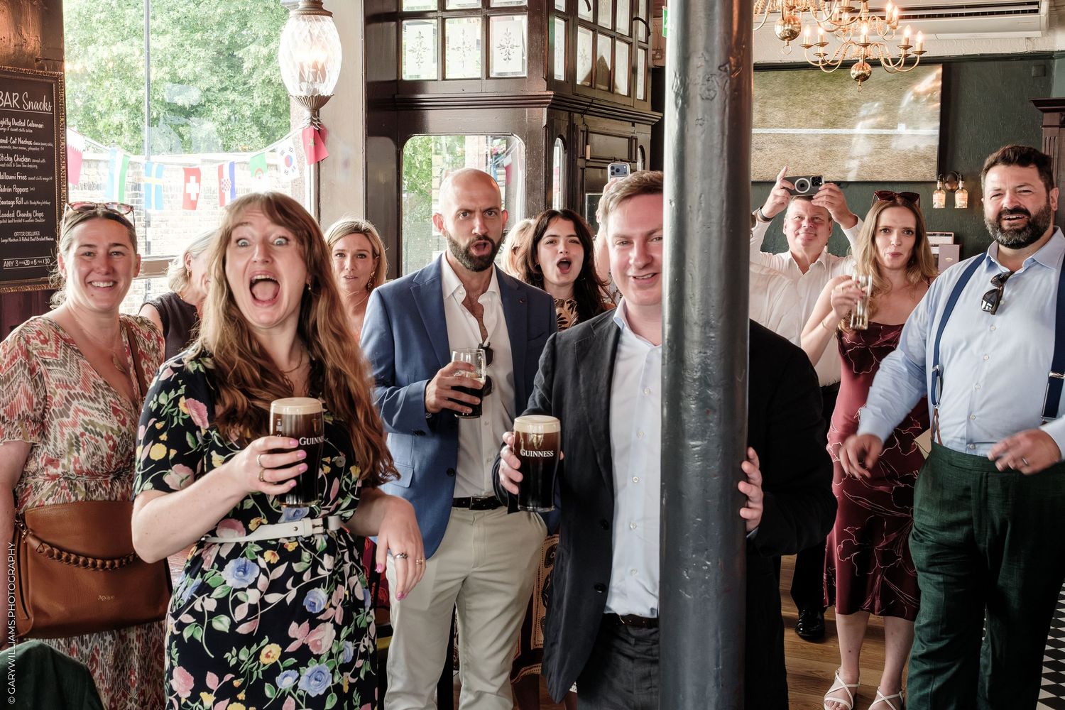 Group of friends laughing and drinking Guinness in a lively pub setting during a social gathering.