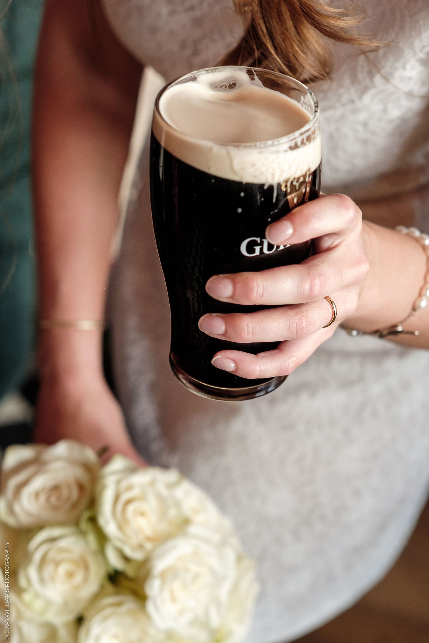 Bride in white dress holding a pint of Guinness beer and a bouquet of white roses at a wedding.