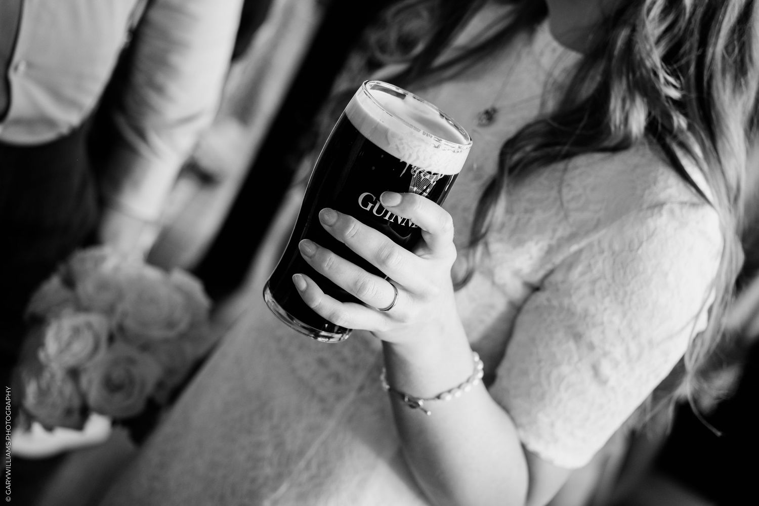 Bride in lace dress holding a pint of Guinness beer at a wedding reception, black and white photo.