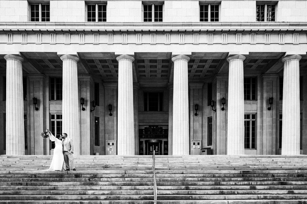 Black and white photo of a couple dancing on grand steps of a neoclassical building with tall columns.