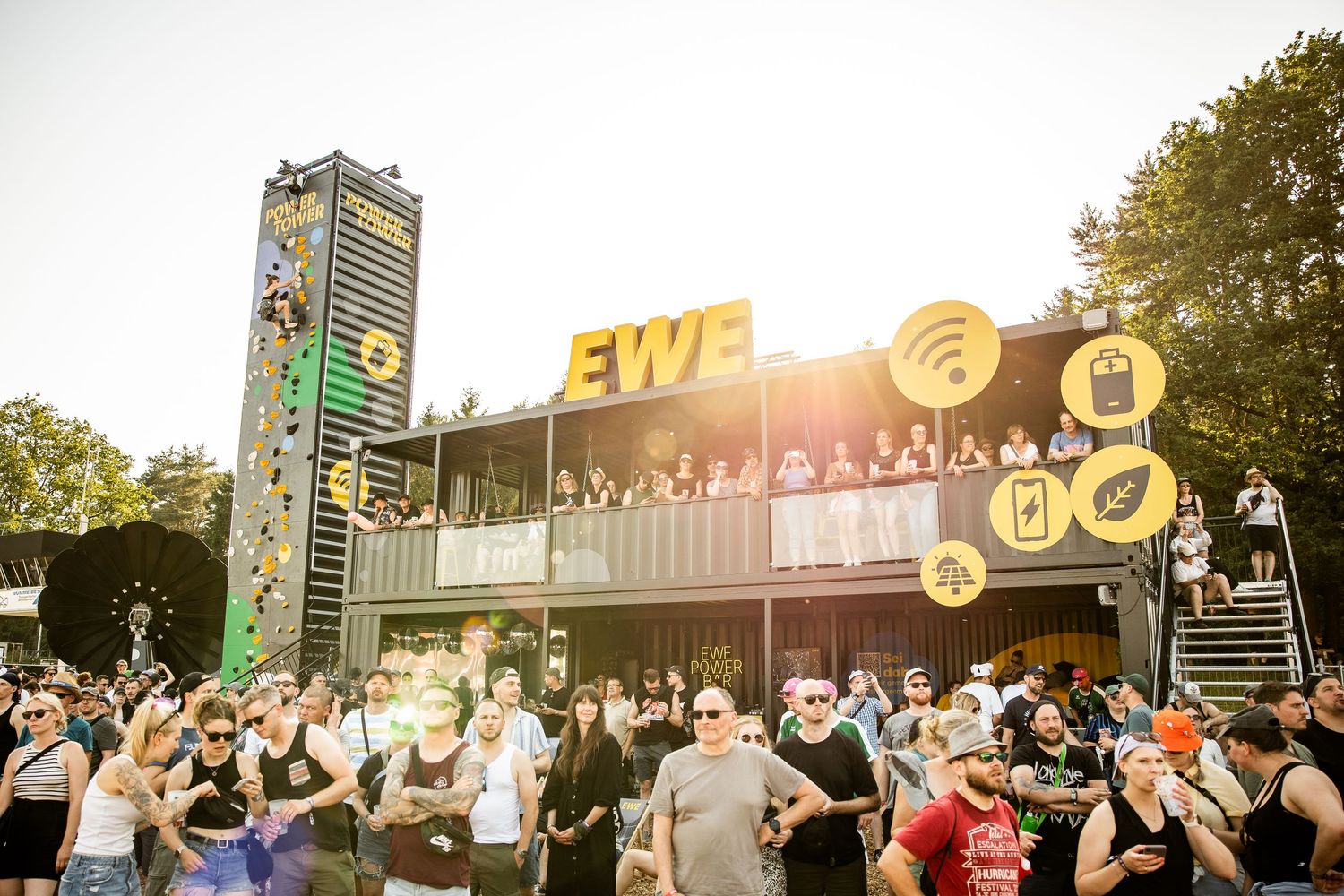 Crowd gathered at an outdoor EWE branded festival stage during a sunny evening event.