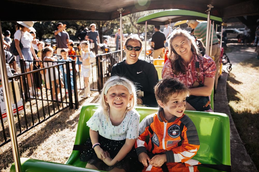 Children and adults enjoy a fun green train ride at a sunny outdoor amusement park event.
