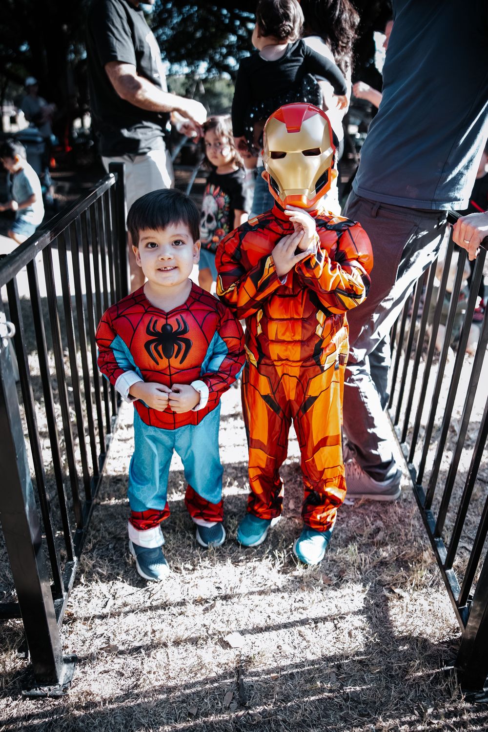 Two children in Spiderman and Iron Man Halloween costumes standing on outdoor steps.