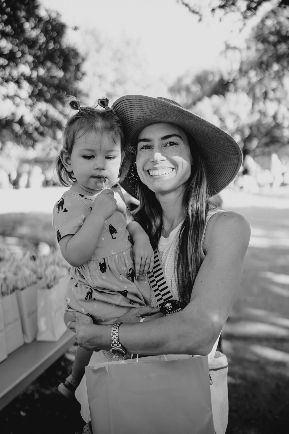 Smiling woman in sun hat holding toddler girl outdoors in black and white photo.
