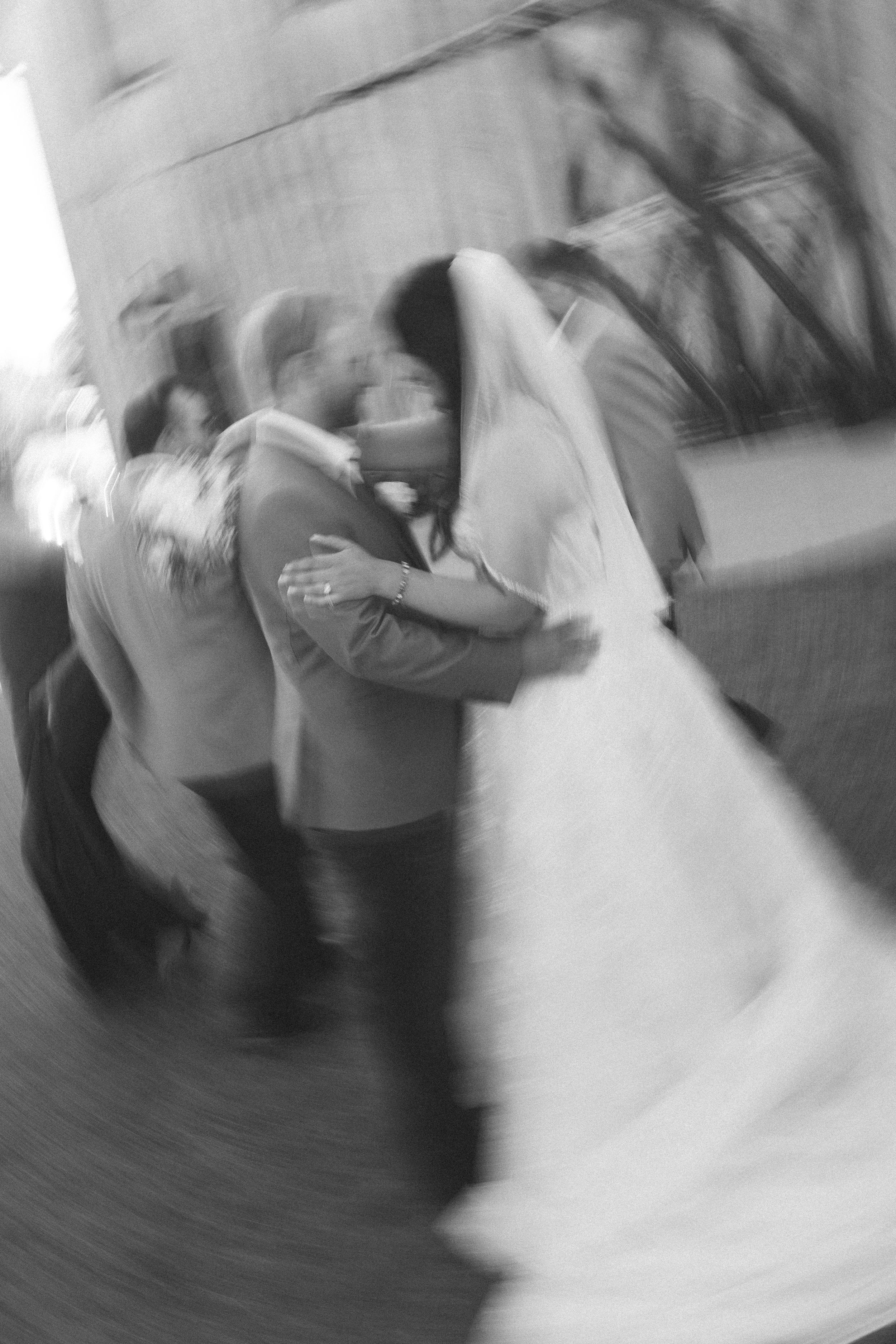 Blurry black and white photo of a bride and groom sharing a first dance kiss at their wedding reception.