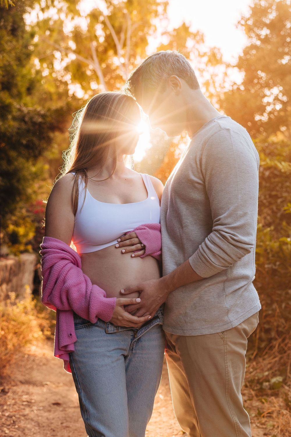 Couple tenderly cradling pregnant belly at golden sunset in nature, maternity photo session outdoors.