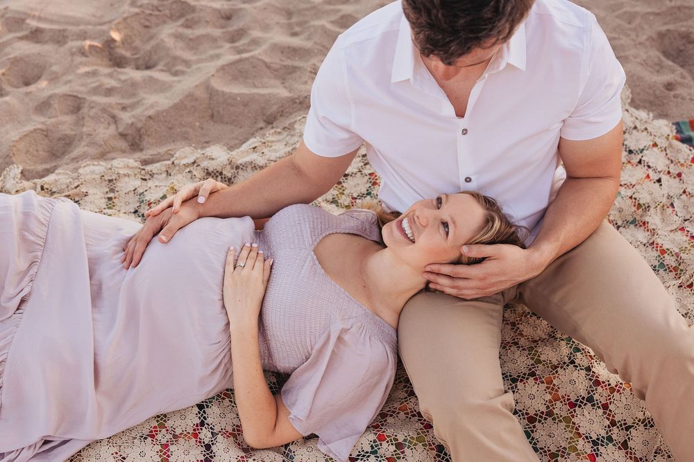 Couple relaxing on a blanket at the beach, woman lying with head on mans lap, smiling up at him.