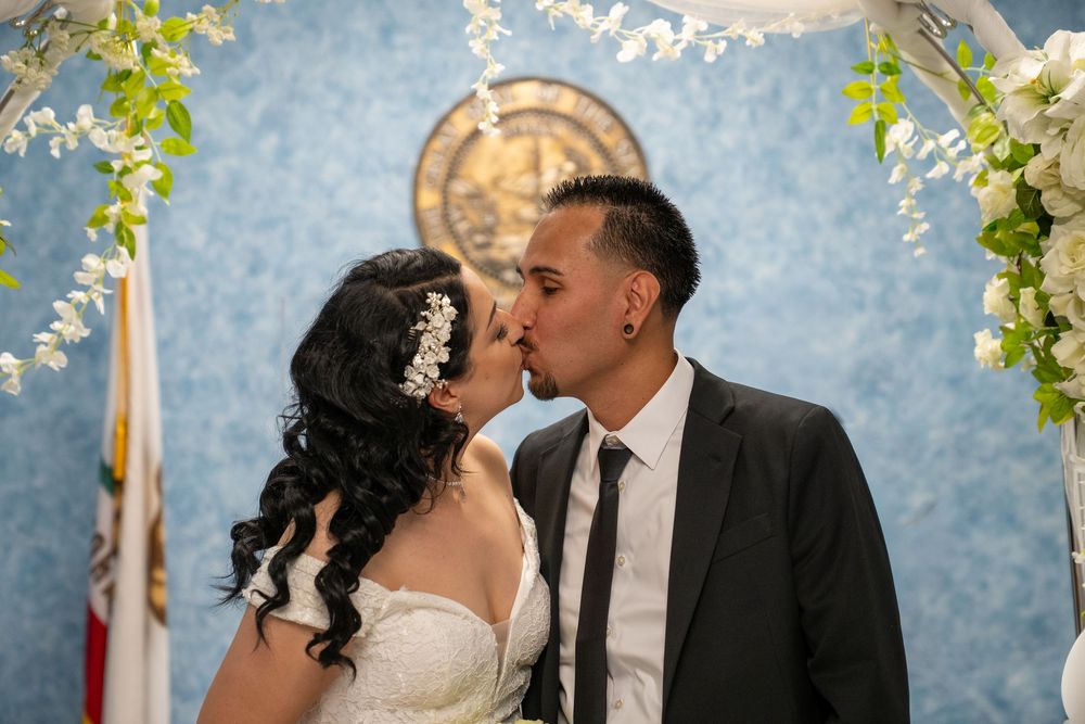 Bride and groom share a kiss at their wedding ceremony under a floral arch with white flowers.