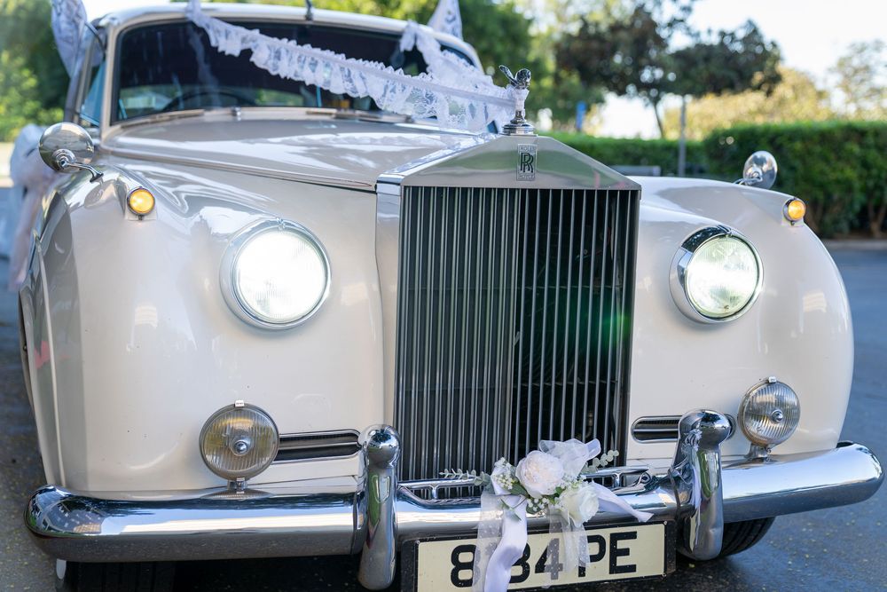 Elegant white Rolls-Royce vintage wedding car decorated with white ribbons and flowers, license plate 834PE.