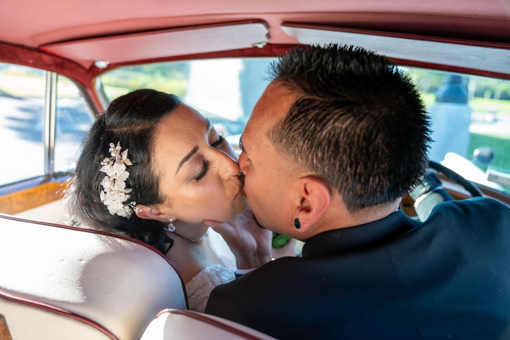 Newlywed couple sharing a romantic kiss inside a vintage car on their wedding day.