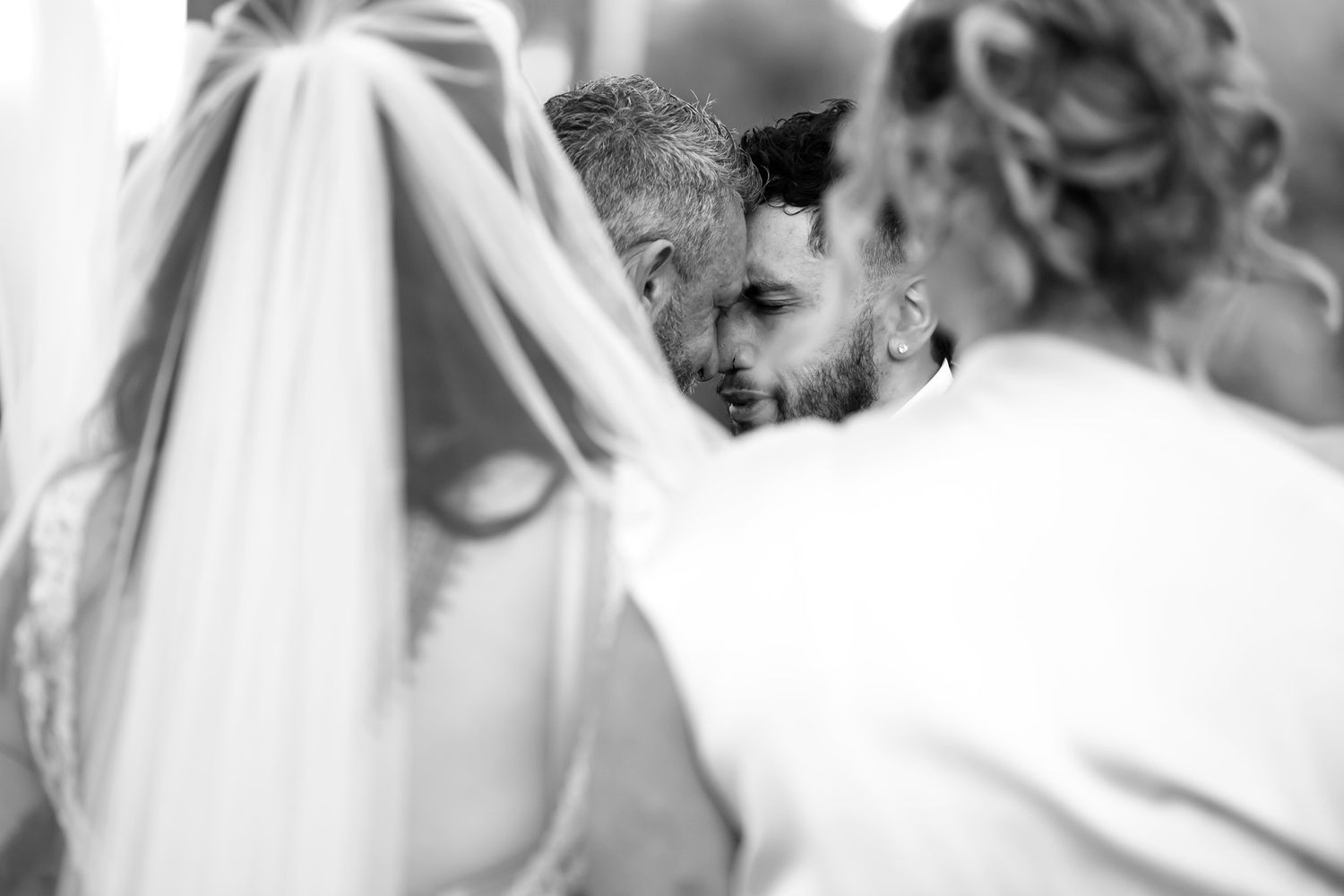 Black and white wedding photo of bride and groom sharing an intimate moment, with veil draped in foreground.