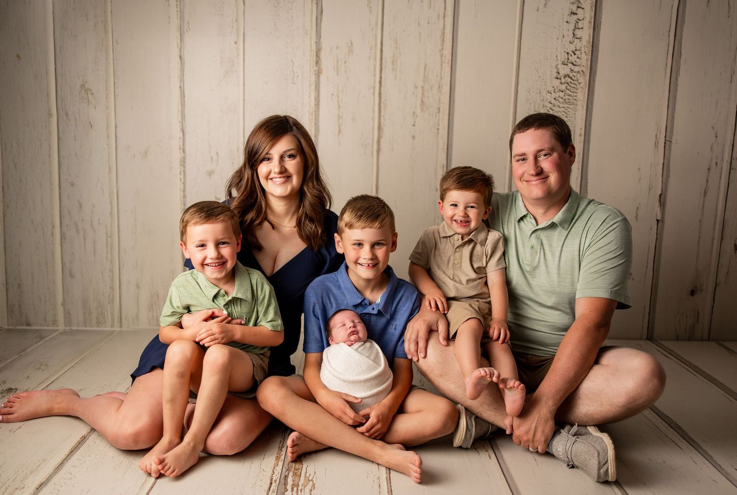Happy family of six posing for a newborn photo session, parents with three young boys and a swaddled baby.