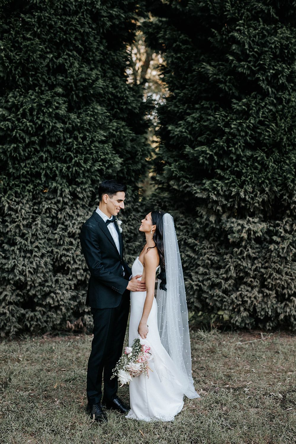 Bride and groom share an intimate moment in front of a lush green ivy wall on their wedding day.
